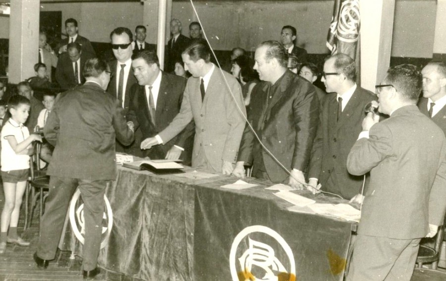 Vicens Calderón fent de presentador en el repartiment de medalles dels 25 anys de socis a la Sala Iris. El podem veure amb el micròfon a la mà. A la foto: Mortes, Aparicio, G.Ros, J.M. Vidal, en el momnet del lliurement en a Gracià Cuesta. Any 1958.