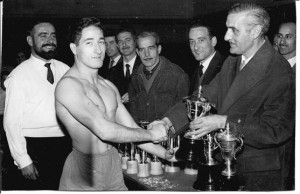 El president de lluita, Sr. Emilio López Jimeno, lliura el trofeu de Campió: a Marià Cortés al febrer de 1960 al Saló Iris de Barcelona participant també un nodrit grup de lluitadors de tots els pesos pertanyents al Barcelonès.